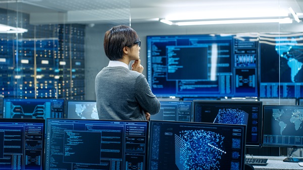 In the System Control Room Technical Operator Stands and Monitors Various Activities Showing on Multiple Displays with Graphics. Administrator Monitors Work of Artificial Intelligence.
